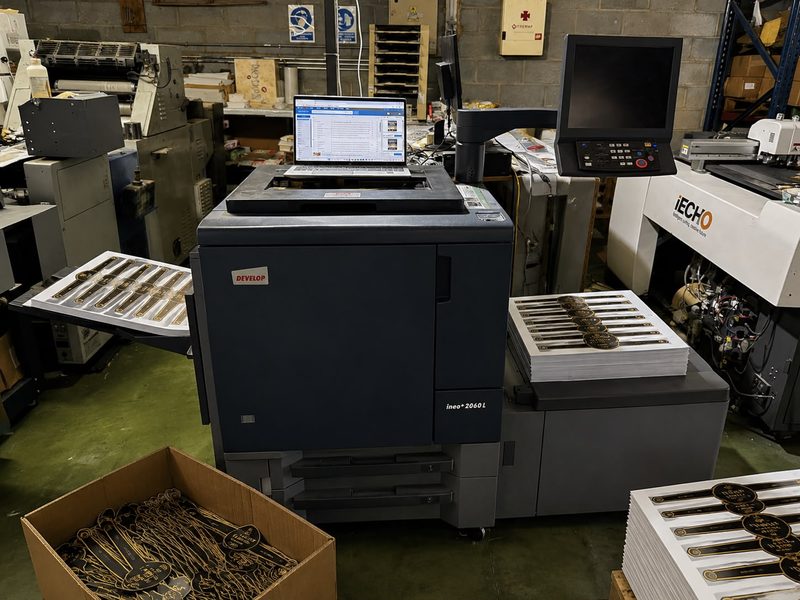 Equipo de impresión digital de producción con pliegos de vitolas impresas y la troqueladora digital al fondo